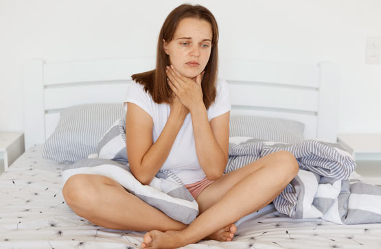 https://www.therapmed.ch/wp-content/uploads/2021/11/sad-unhappy-sick-woman-with-dark-hair-wearing-white-casual-t-shirt-sitiing-on-bed-with-crossed-legs-touching-her-neck-suffering-from-sore-throat-frowning-face.jpg